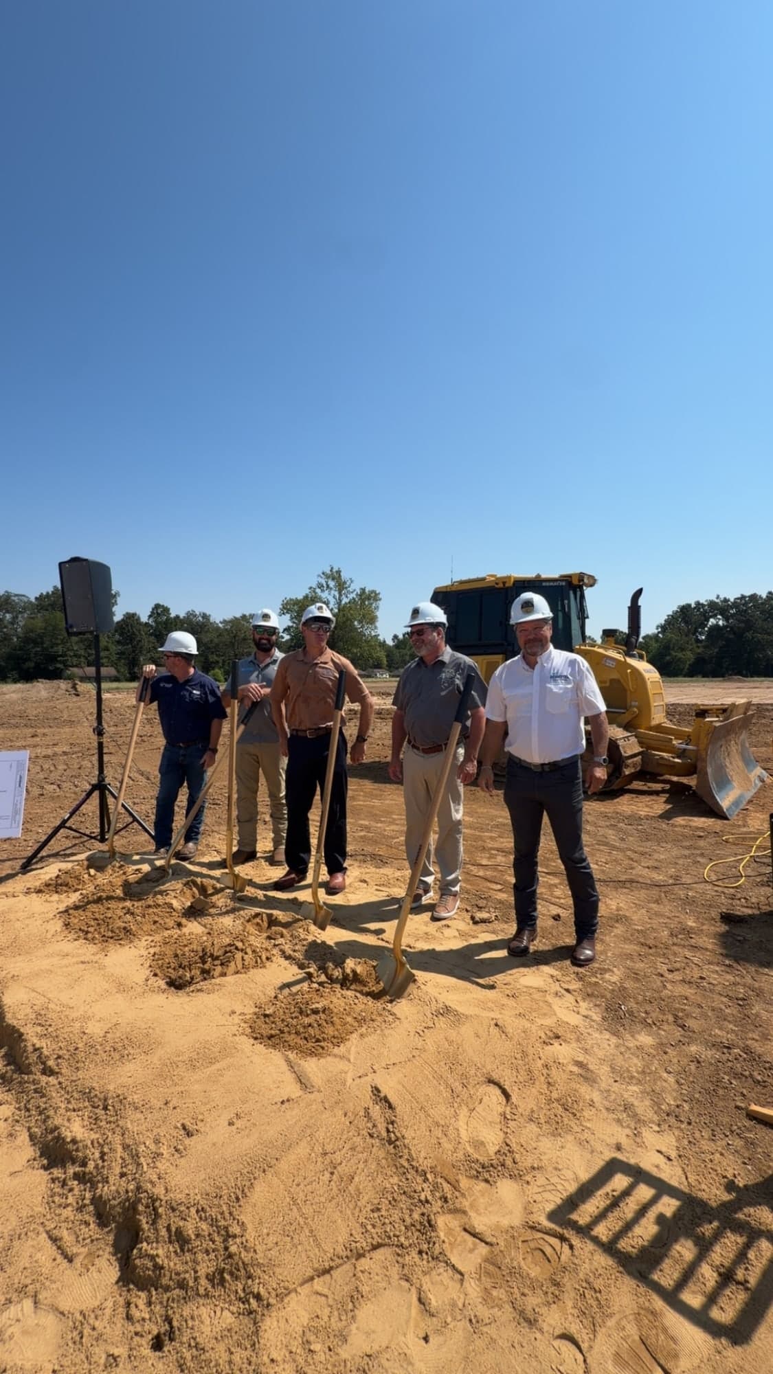 Groundbreaking participants standing near construction equipment